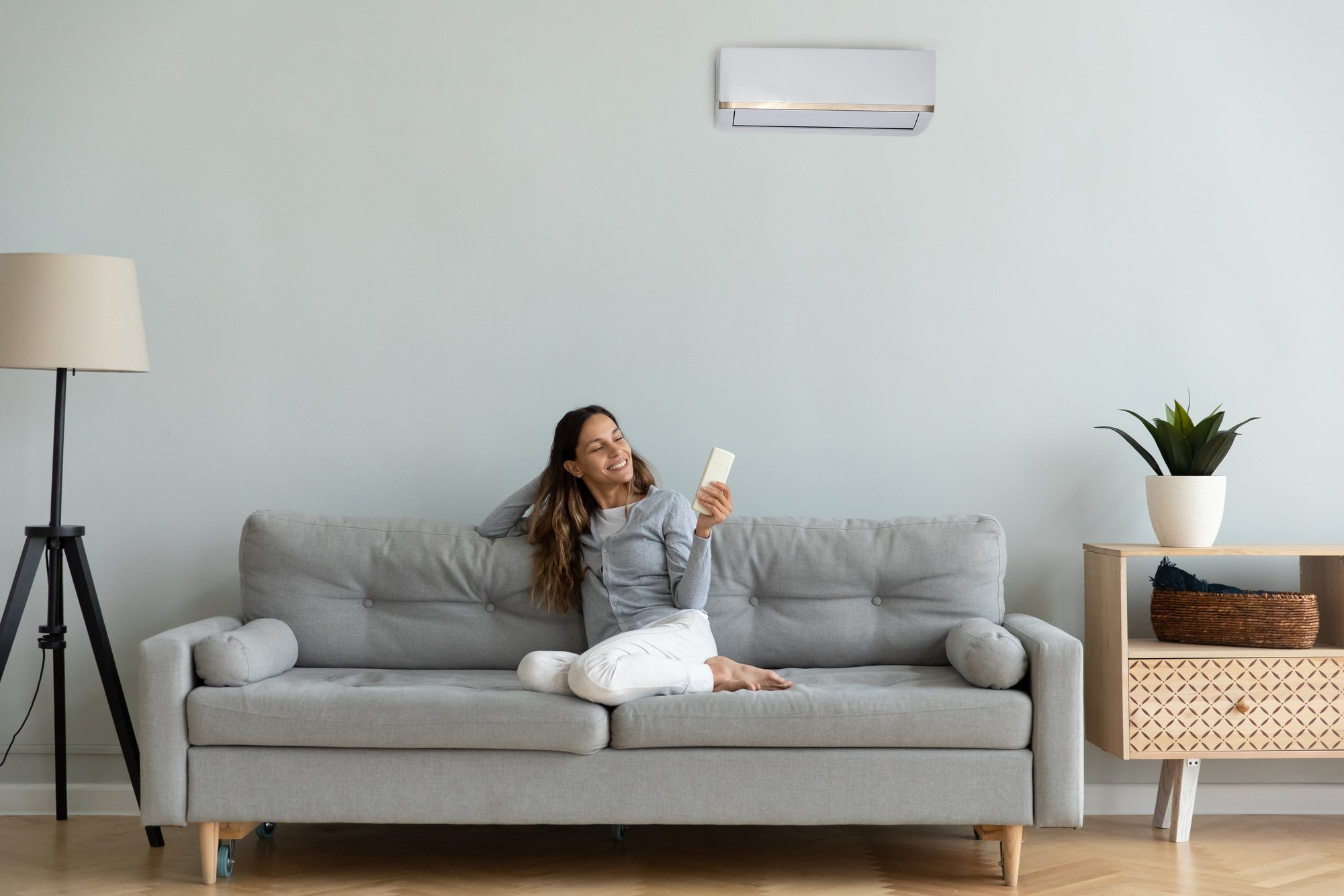 Woman holding remote control manages degrees enjoy air-conditioned flat